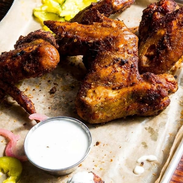 Crispy, seasoned chicken wings with dipping sauce, pickled onions, and jalapeños on a tray.