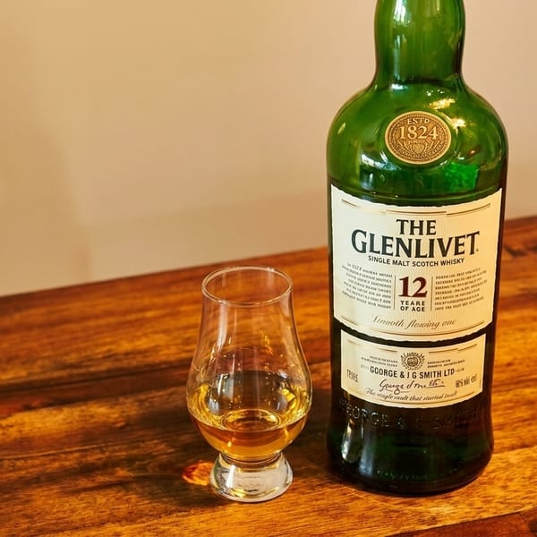 A bottle of The Glenlivet 12-year-old single malt scotch whisky next to a glass of whisky.